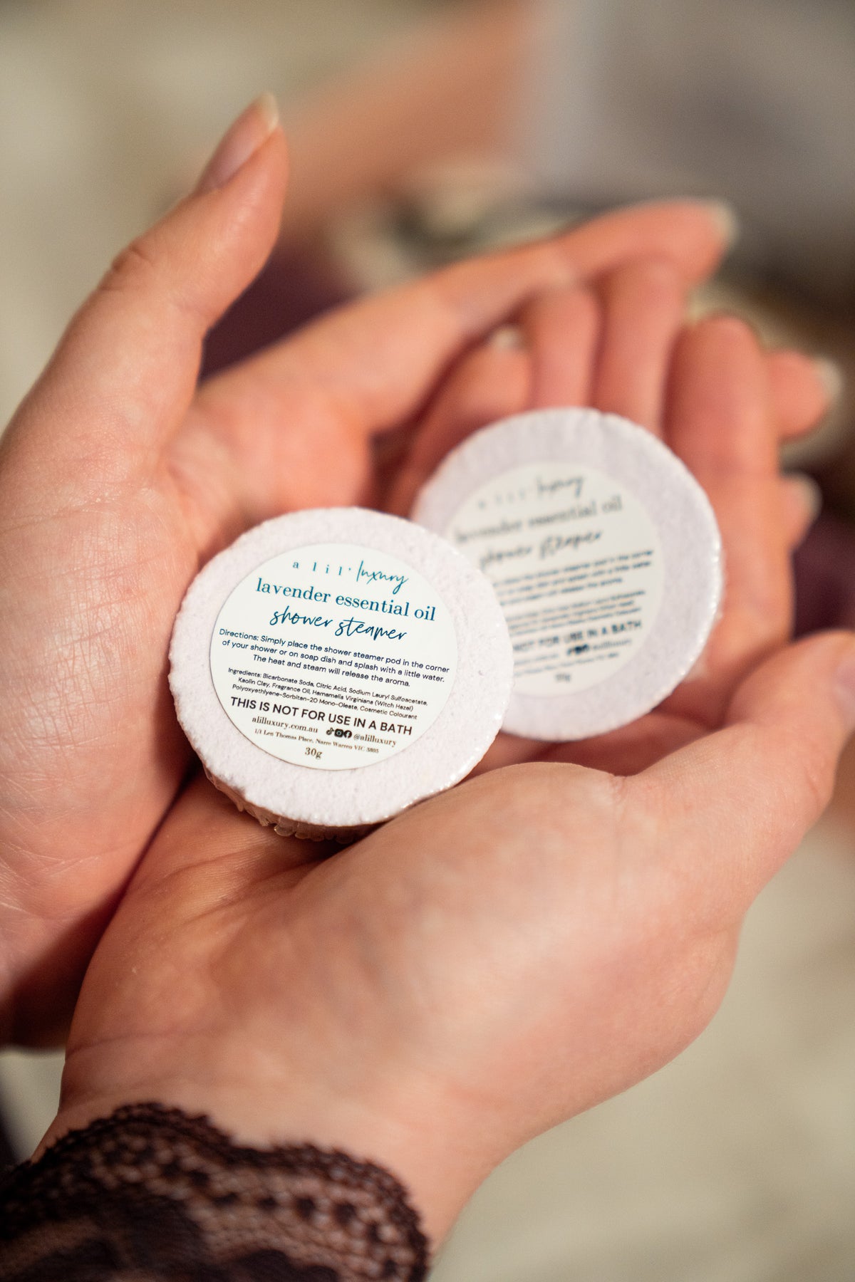 Two small round white jars of honey lavender essential oil hand and foot soaks held in a person's hands, with the front jar label clearly showing the brand and product name.