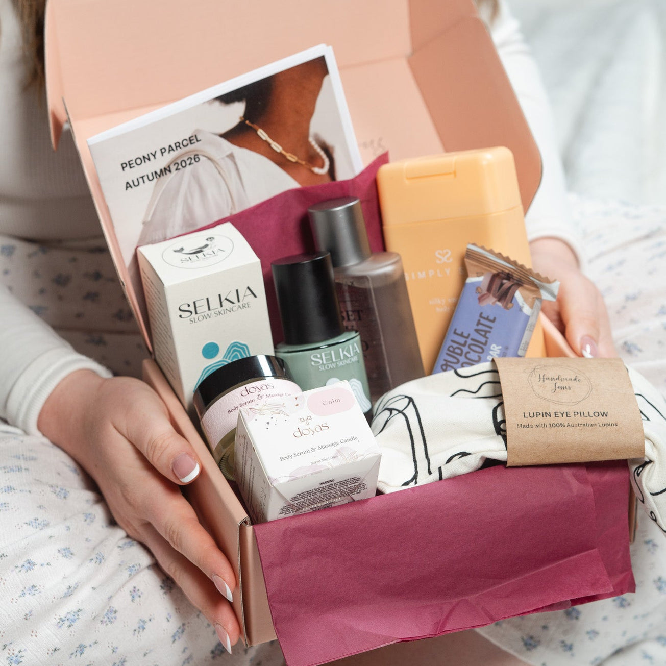 Person holding a box of beauty products including skincare items and a perfume bottle.